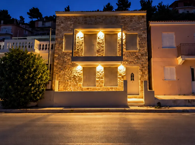 Πέτρινη πρόσοψη με φωτιστικά τοίχου το βράδυ